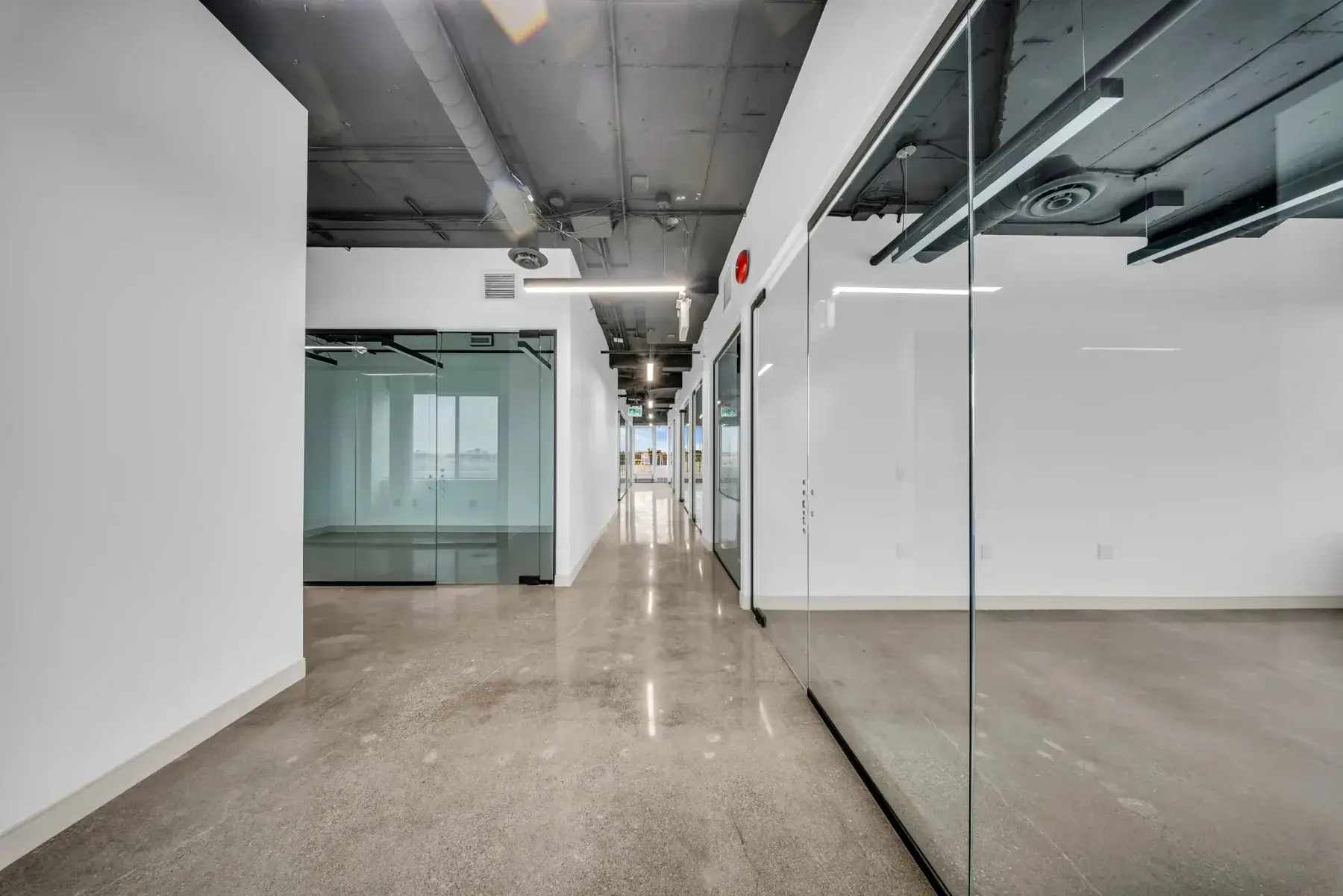Sunlit corridor lined with glazed offices and polished concrete flooring at Workplace K, 1940 Eglinton Ave, Scarborough